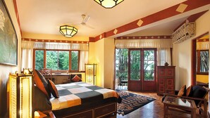 A spacious bedroom with a large bed, a desk, and a chair. There are multiple windows providing natural light and views of the outdoors. - Norling House (Dharamshala)