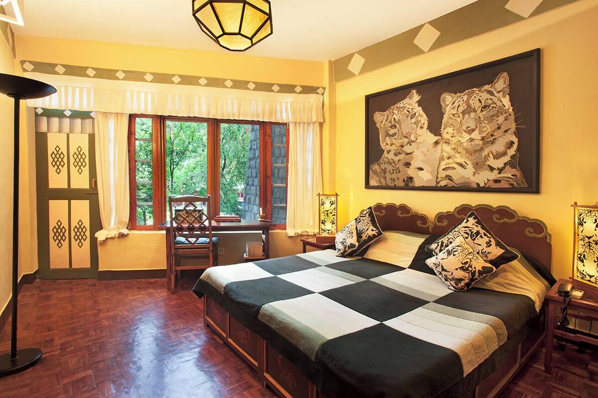 A bedroom with a large bed, a window with curtains, a desk, and a chair.