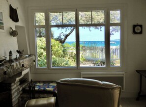 A room with a large window offering a view of the sea and a wooden deck.