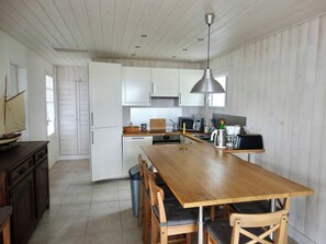 A kitchen with a wooden table, white cabinets, and a hanging light fixture.