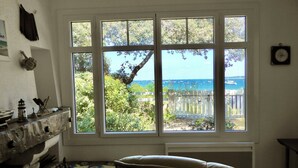 Een kamer met een groot raam dat uitkijkt over een strand, een open haard en een stoel.