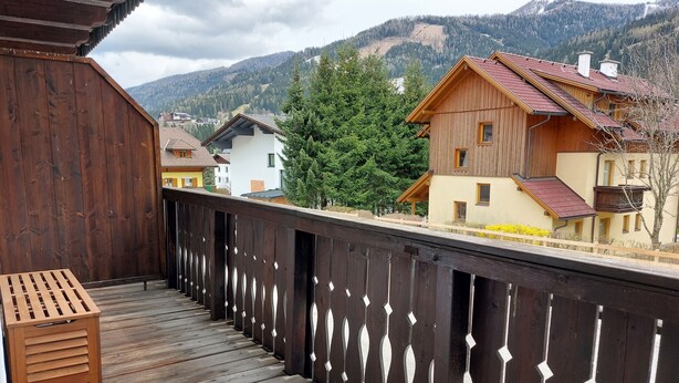 A wooden balcony with a slatted railing overlooking a mountainous landscape.