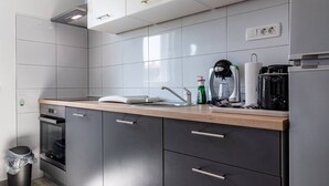 A modern kitchen with grey cabinets, a wooden countertop, a coffee machine, and a trash bin. - Holiday Home Sunny Side (Kastela)