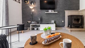 A modern living room with a flat-screen TV, a fireplace, and a round coffee table with pastries. - Holiday Home Sunny Side (Kastela)