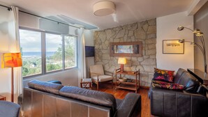 A living room with a stone wall, a sofa, a chair, a lamp, and a view of the sea. - La Entretenida -  View and Sound of the Sea, Next to the Beach. Pet-Friendly. (Doniños Ferrol)
