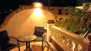 Une terrasse extérieure avec une table ronde et deux chaises, un mur décoratif et un palmier.