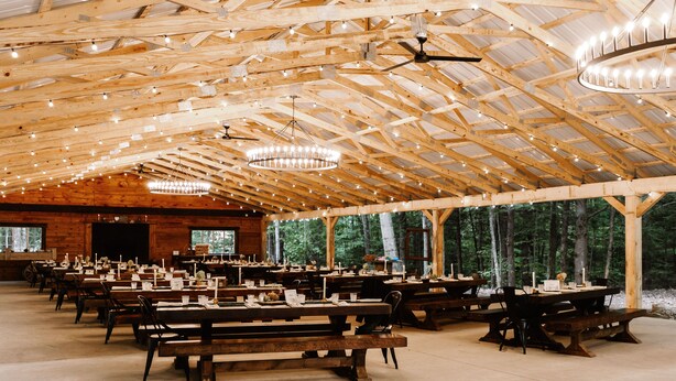 Un grand espace de restauration couvert, doté de tables et de bancs en bois, de guirlandes lumineuses et d’un plafond haut avec des poutres apparentes.