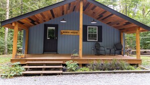 Une petite cabane rustique, portant l’inscription « Noble House », avec une véranda en bois, deux chaises et une petite table.