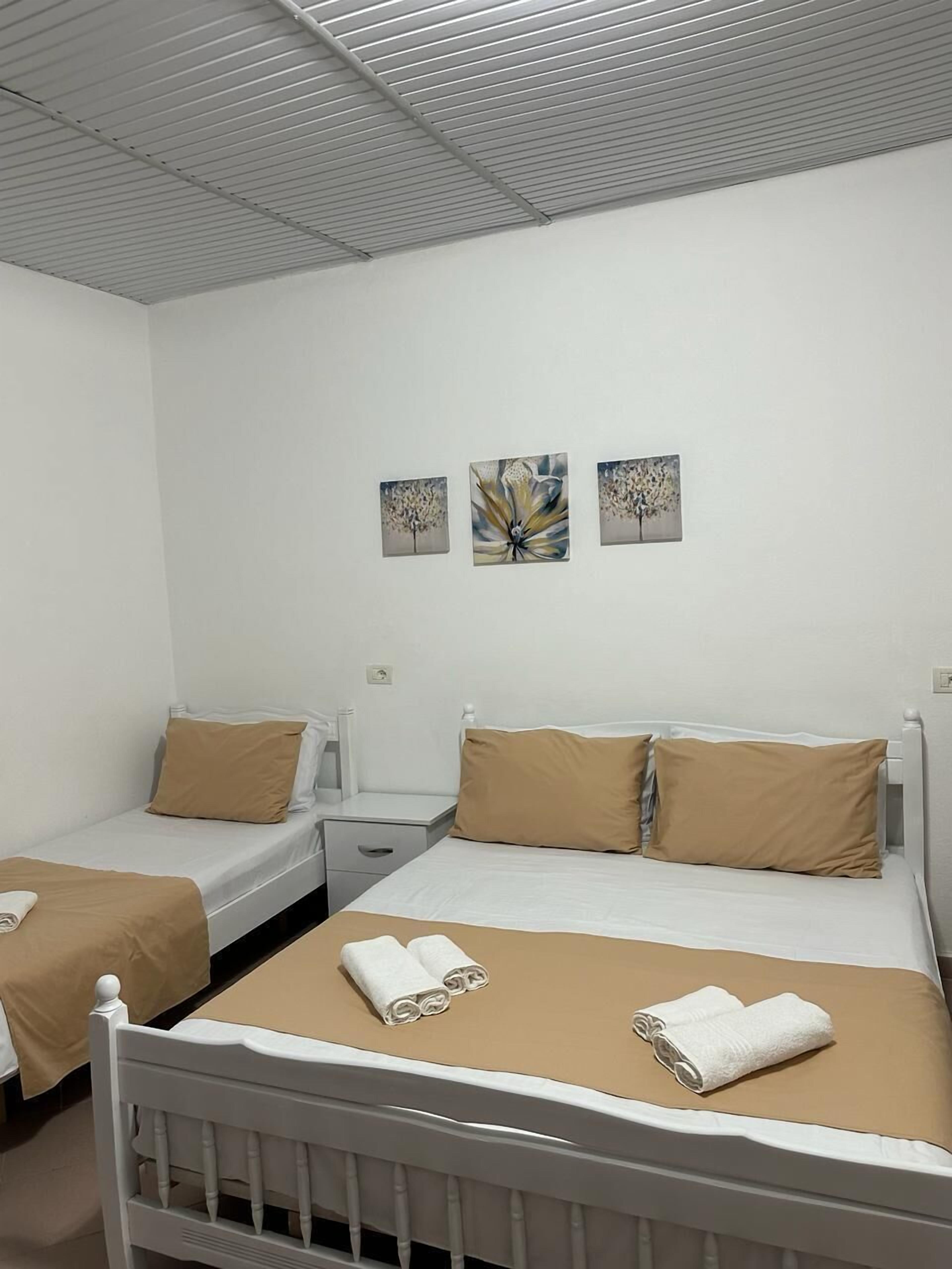 Hotelkamer met twee enkele bedden, een groot bed en een nachtkastje. Drie schilderijen hangen aan de muur.