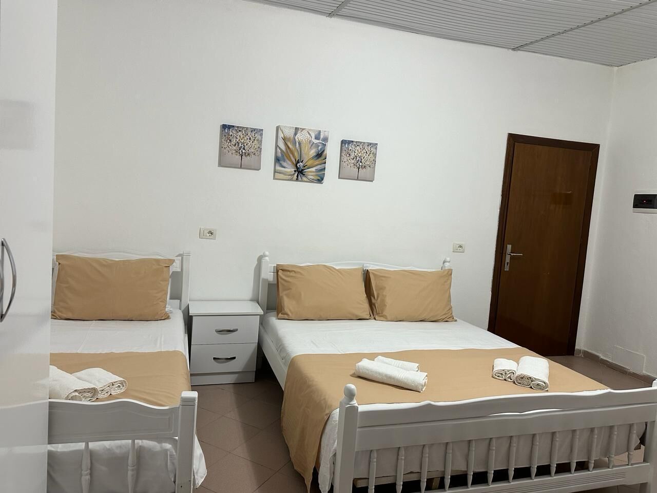 Hotellihuone, jossa on kaksi sänkyä, puinen pääty, yöpöytä ja yölamppu sekä ovi.