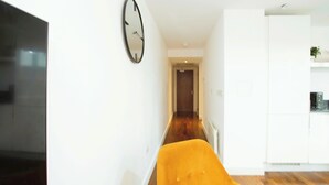 Ein modernes Interieur mit Holzboden, einem leuchtend gelben Sessel, einem großen Flachbildfernseher und einer Küchenzeile mit weißen Schränken.