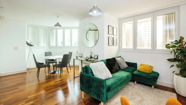 Ein modernes Wohnzimmer mit einem grünen Sofa, einem Essbereich mit einem Glastisch und großen Fenstern.