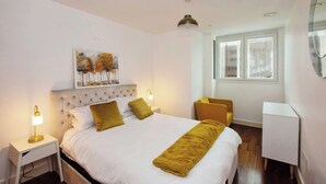 Ein Hotelzimmer mit Bett, Nachttischen, einem Sessel, einem Schreibtisch und einem Bild an der Wand.