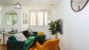 Ein modernes Wohnzimmer mit einem grünen Sofa, einem gelben Sessel, einem runden Spiegel und einem großen Fenster.