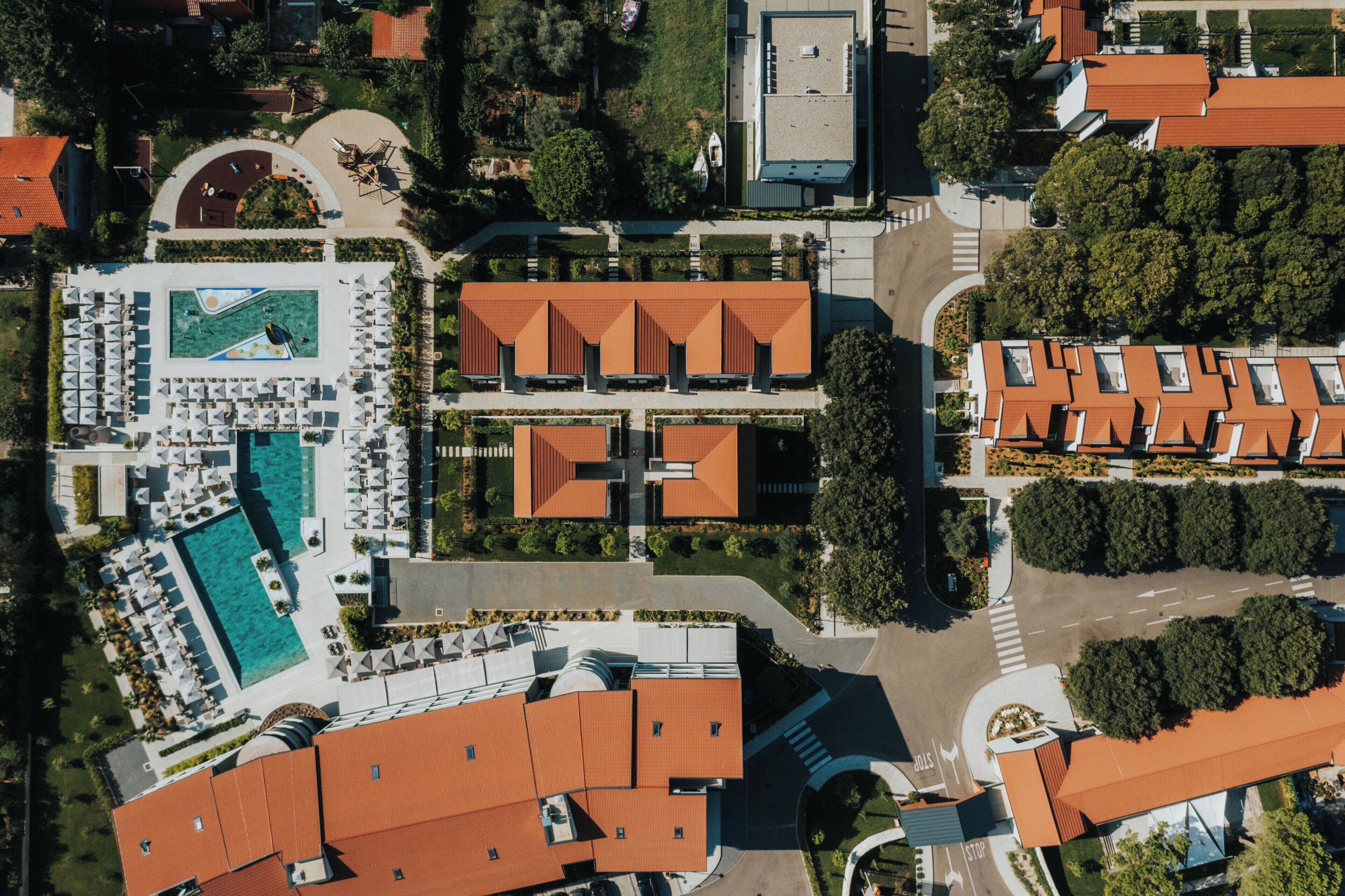 An aerial view of a resort with a swimming pool, multiple buildings with red roofs, and landscaped areas.