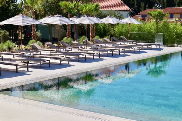 A poolside area with sun loungers and striped umbrellas, surrounded by palm trees and a clear pool. - Molum Hotel & Residences (Sveti Filip i Jakov)