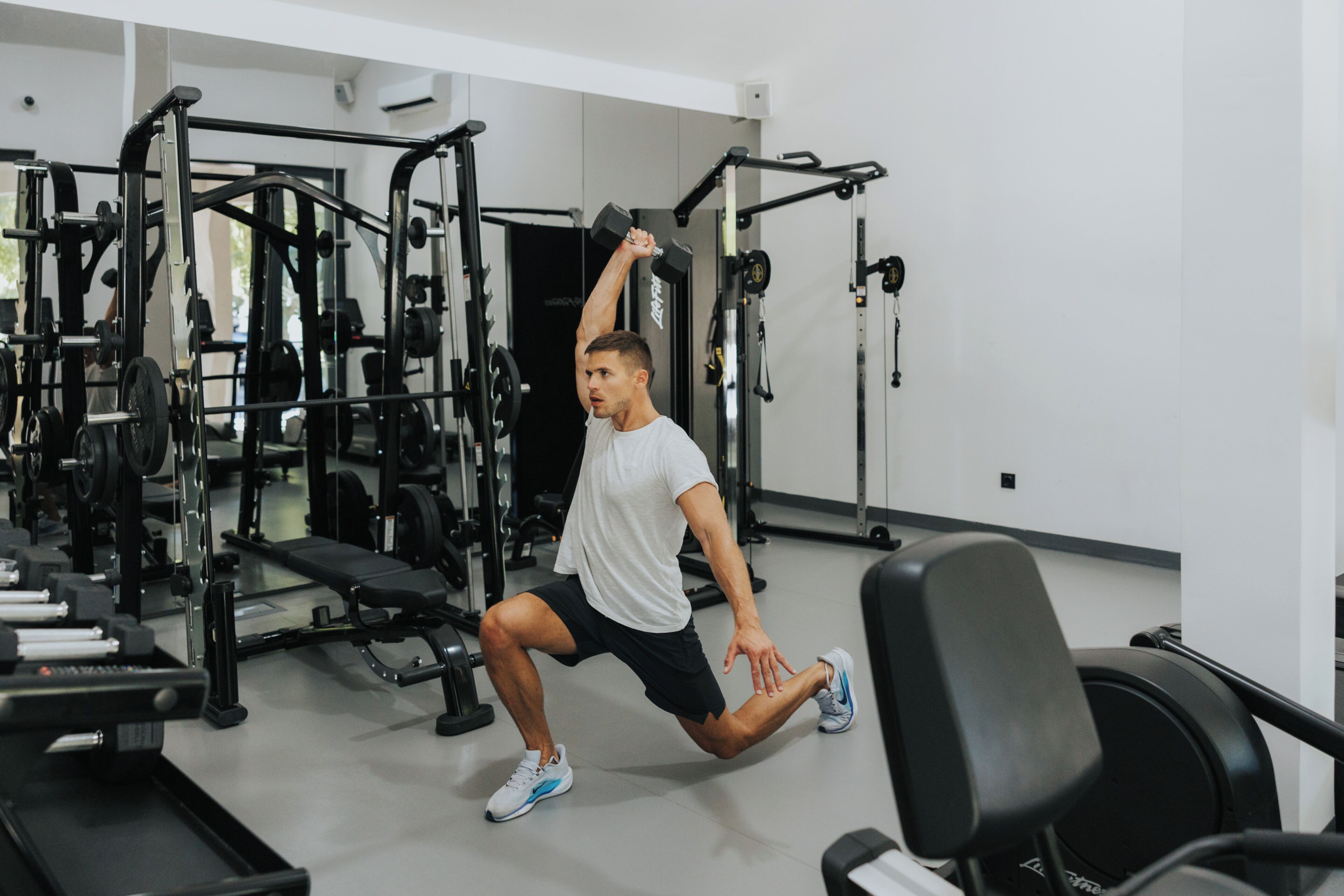 Un gimnasio con equipamiento de levantamiento de pesas, una jaula para sentadillas y una banca.