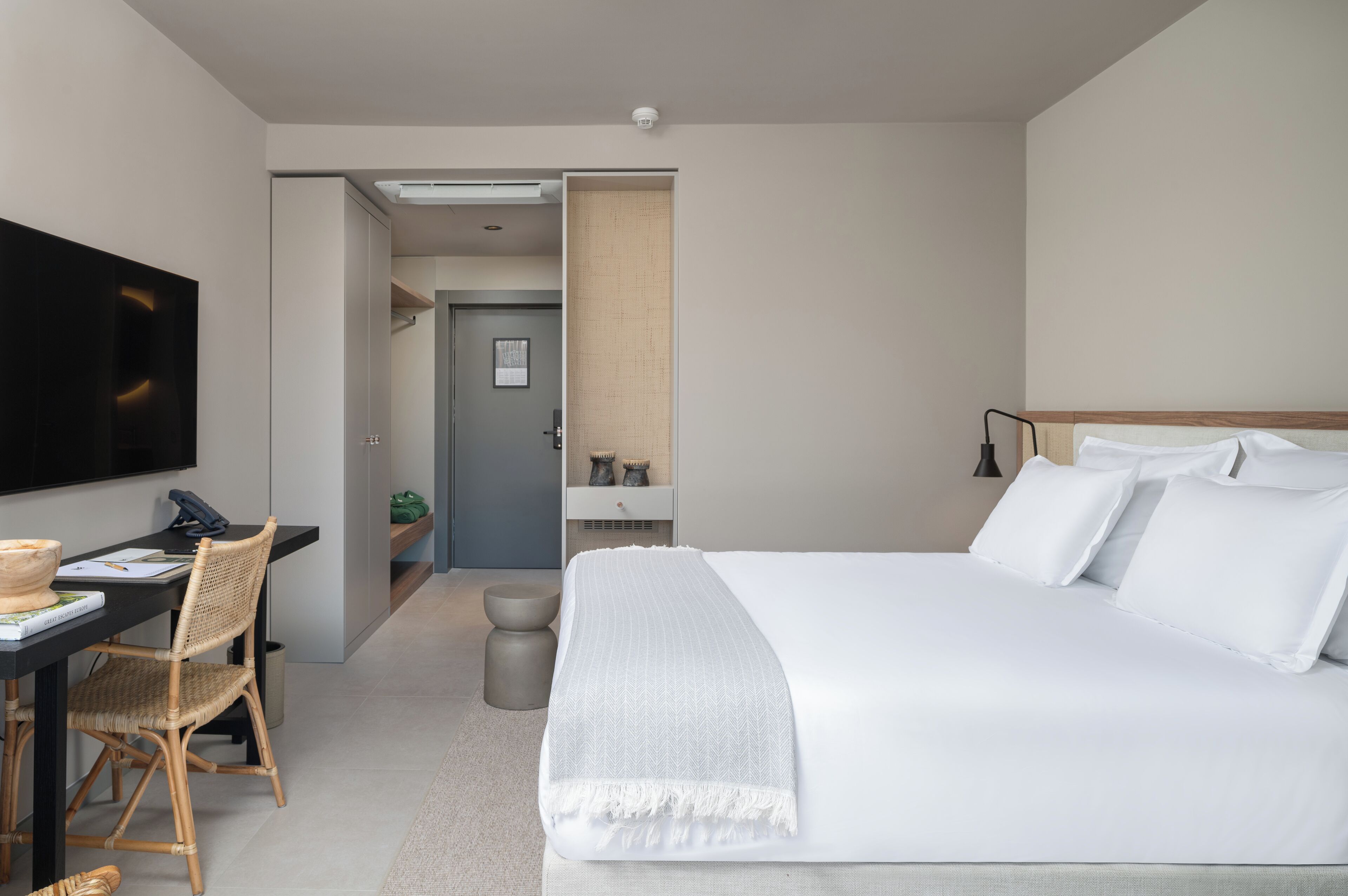 A modern hotel room with a large bed, a desk with a chair, a flat-screen TV, and a small seating area with a chair and a table.