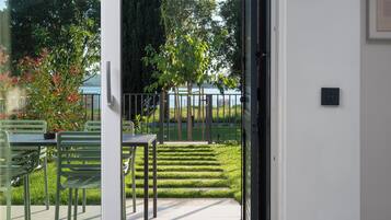A patio area with a table and chairs, a small garden with a tree, and a view of the sea through a glass door.