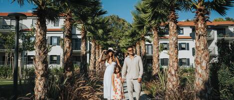 A family walking on a pathway surrounded by palm trees and buildings with balconies.