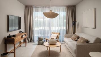 A modern living room with a sofa, a round wooden coffee table, a wicker chair, and a television on a wooden stand.