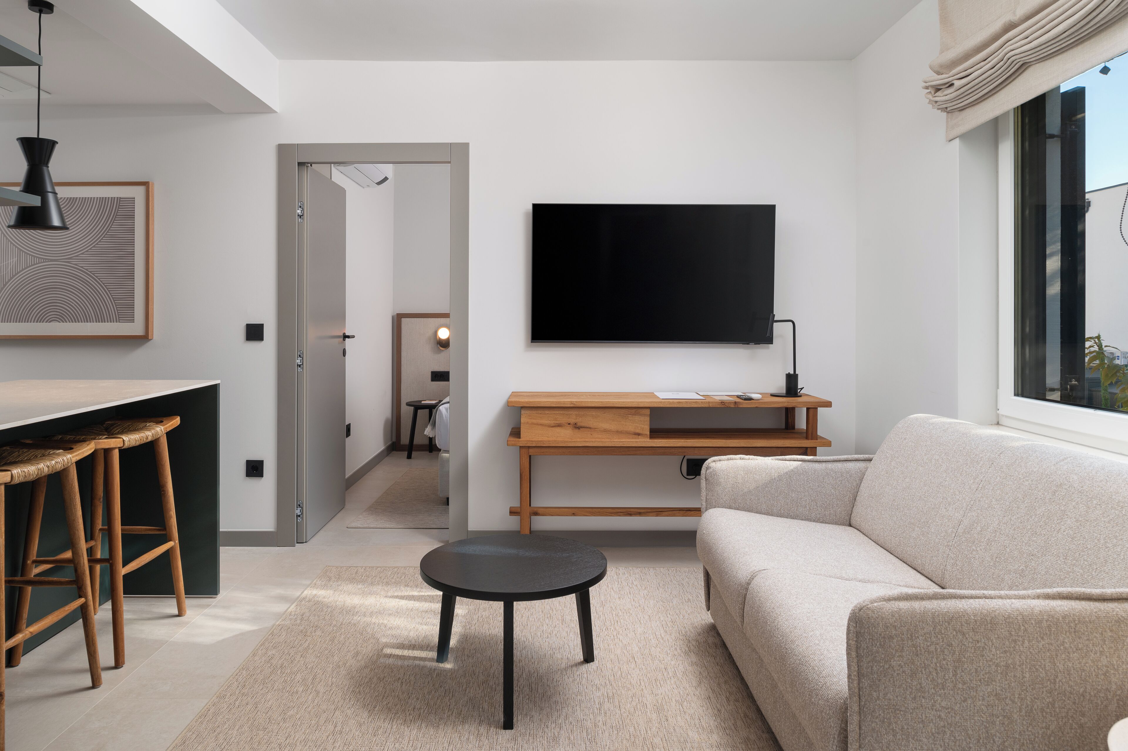 Una sala moderna con un sofá, una mesa de centro, un televisor montado en la pared y un comedor con taburetes.