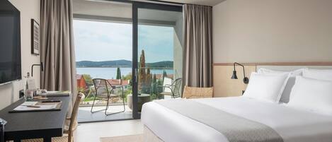 A hotel room with a large bed, a desk with a chair, a TV, and a view of the outdoors.