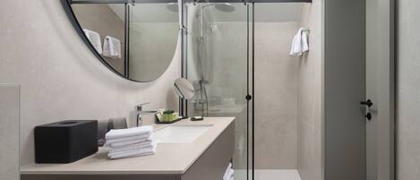 Une salle de bain moderne avec une douche à parois de verre, un miroir rond et un lavabo agrémenté de serviettes soigneusement pliées.