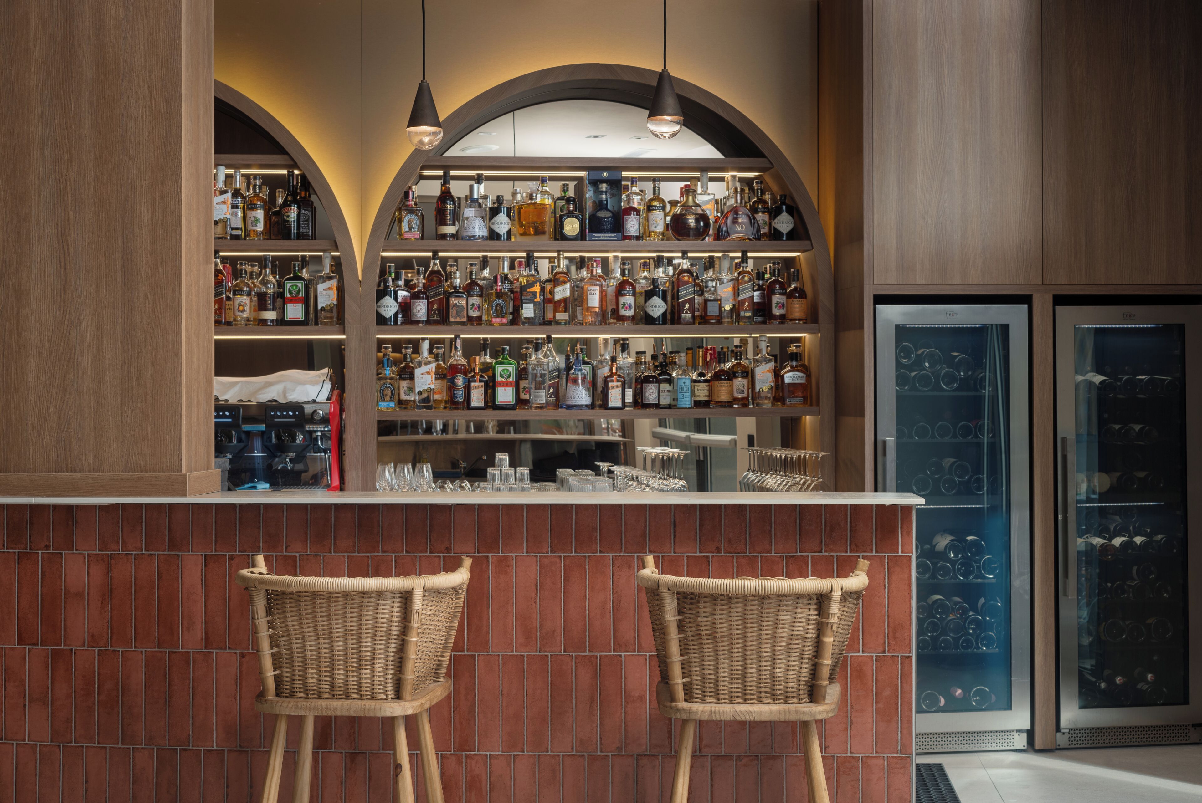A bar area with two wicker chairs, shelves of liquor bottles, and a refrigerated display case.
