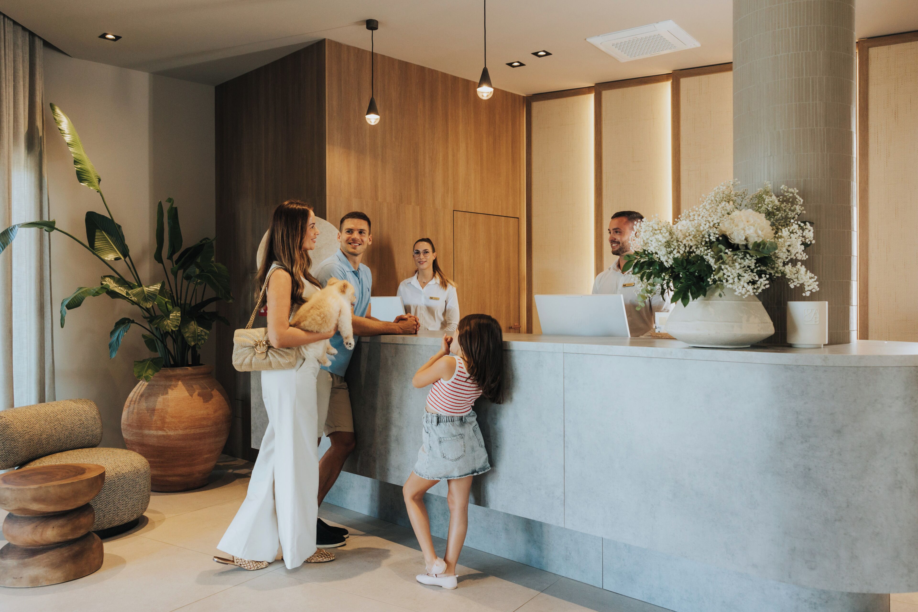 A reception area with a wooden reception desk, a large potted plant, and a seating area with round wooden stools.