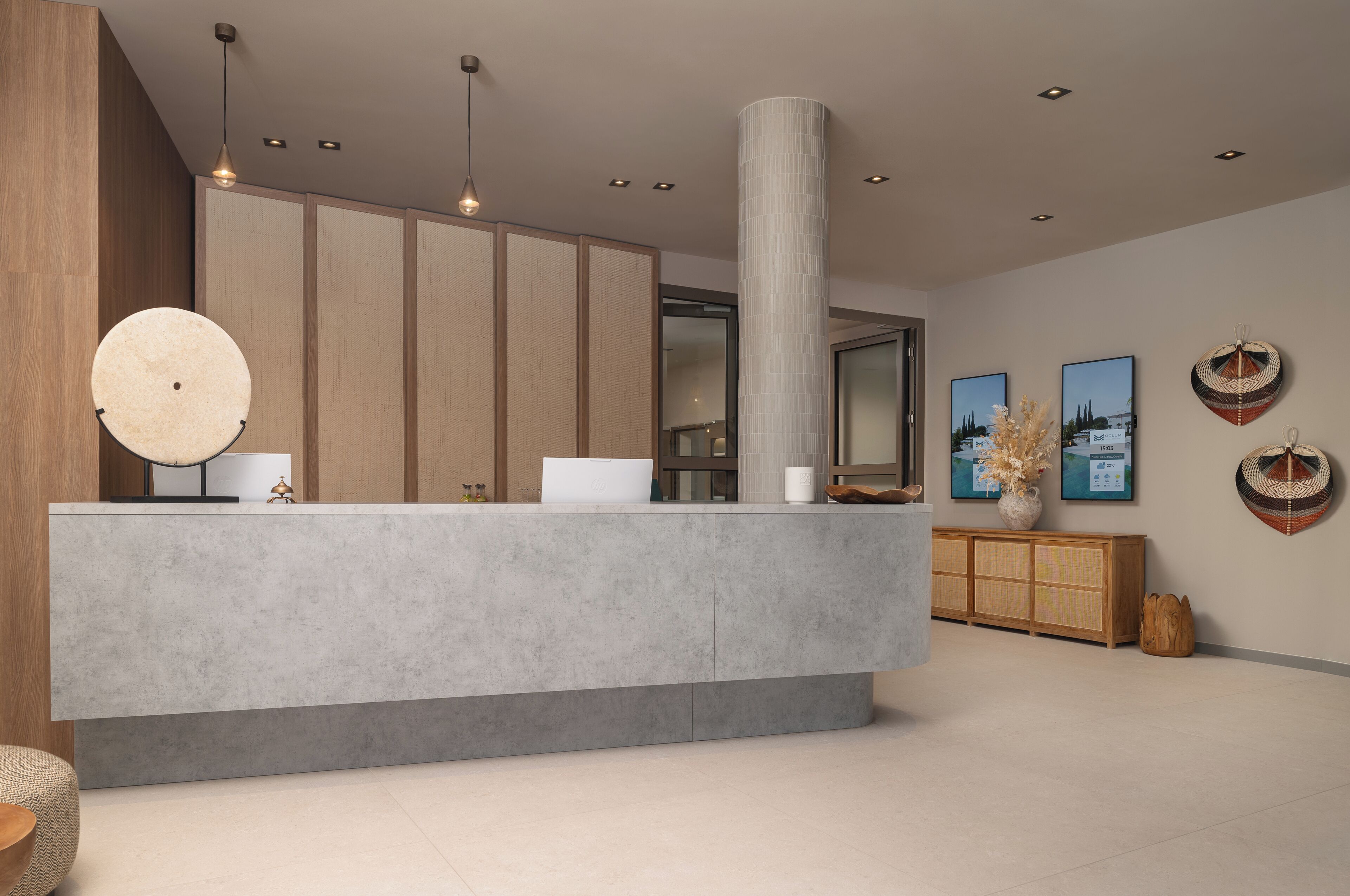 A reception area with a concrete counter, wooden panel walls, and a large pillar. There are framed pictures on the wall and a wooden cabinet with decorative items.