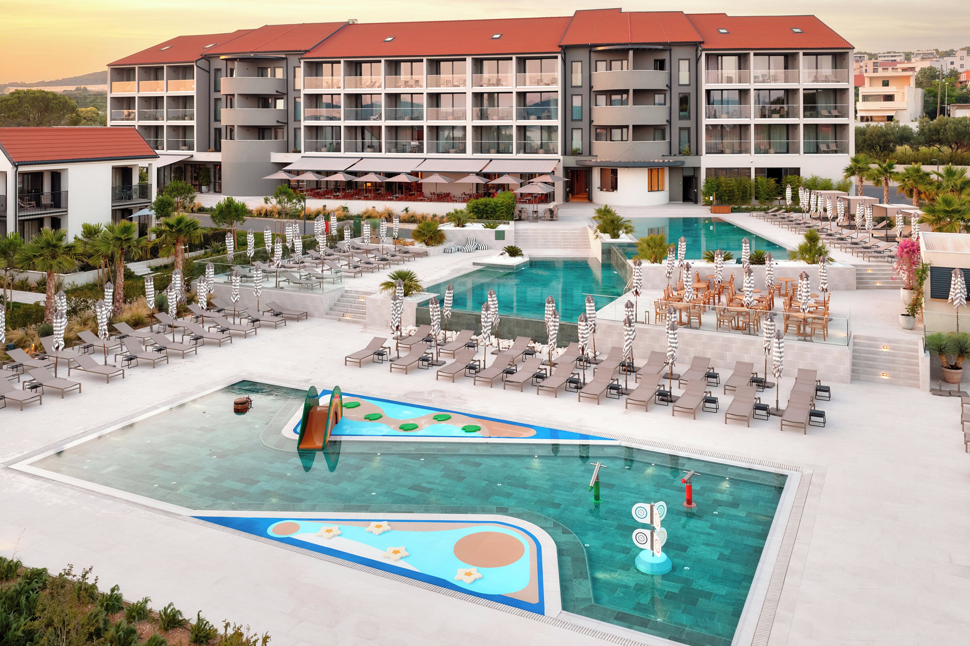 Ein Hotel mit mehreren Schwimmbecken, Liegestühlen und Sitzbereichen im Freien.