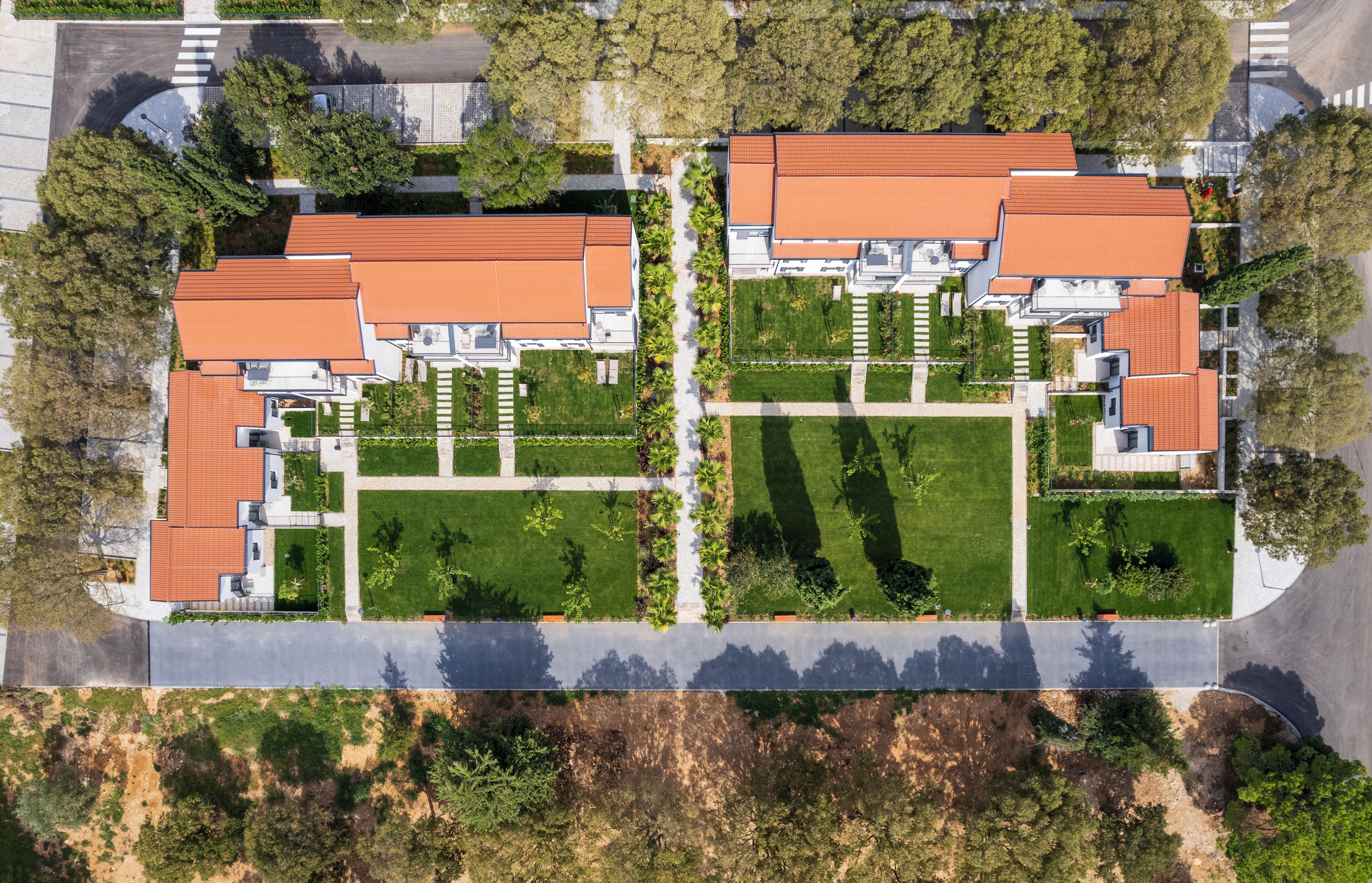 Vista aérea de un área residencial con varias casas, cada una con techo de tejas rojas y rodeadas de céspedes cuidados y árboles.