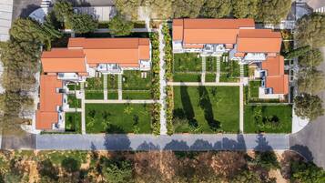 Vista aérea de un área residencial con varias casas, cada una con techo de tejas rojas y rodeadas de céspedes cuidados y árboles.