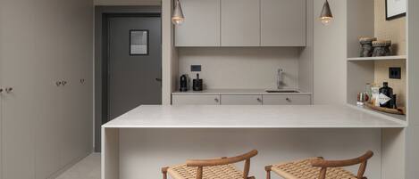 A modern kitchen with a central island, two wooden bar stools, pendant lighting, and a view into the adjacent room.