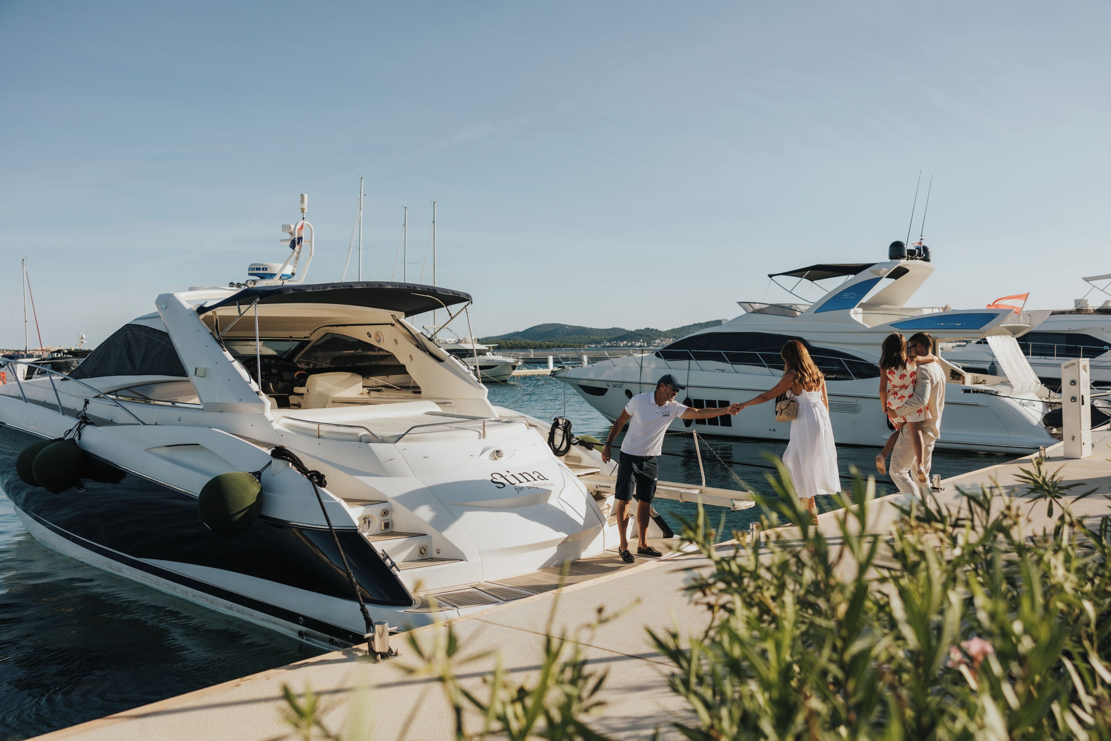 Marina com barcos atracados, céu claro e algumas pessoas passando.