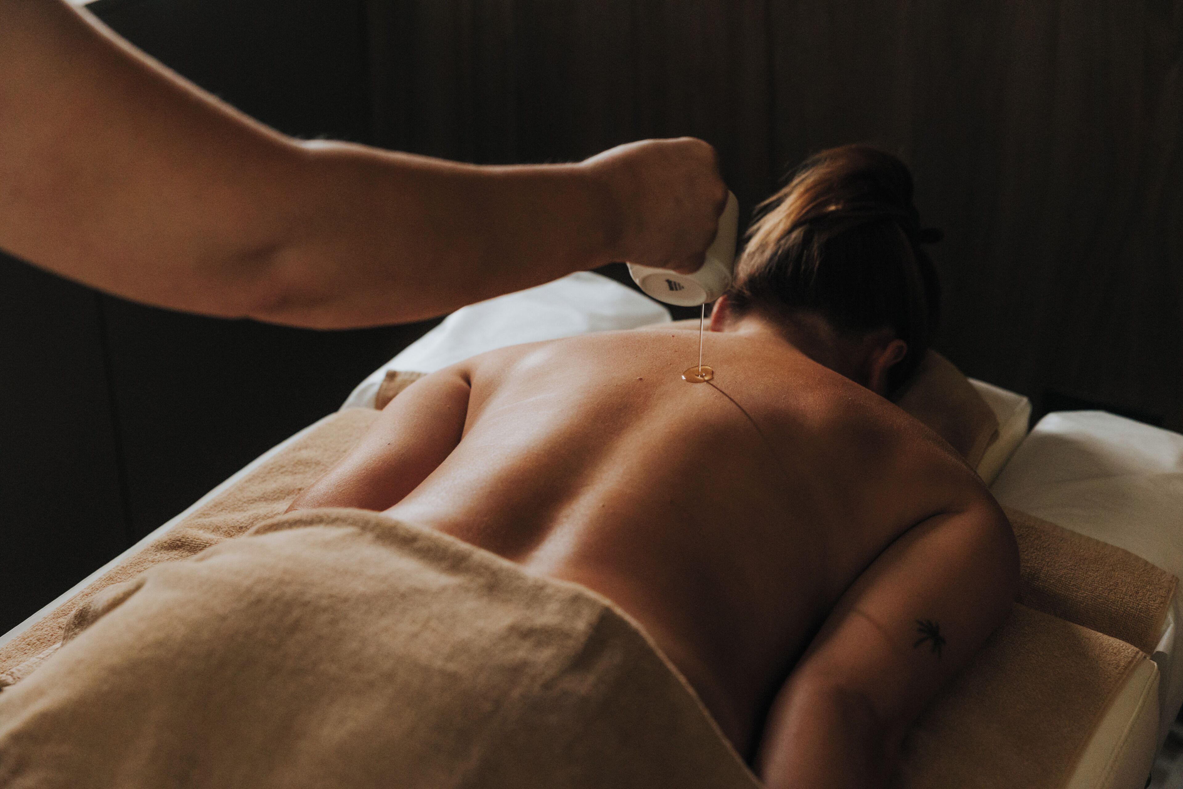 A person receiving a back massage in a room with a wooden wall and a white bed.