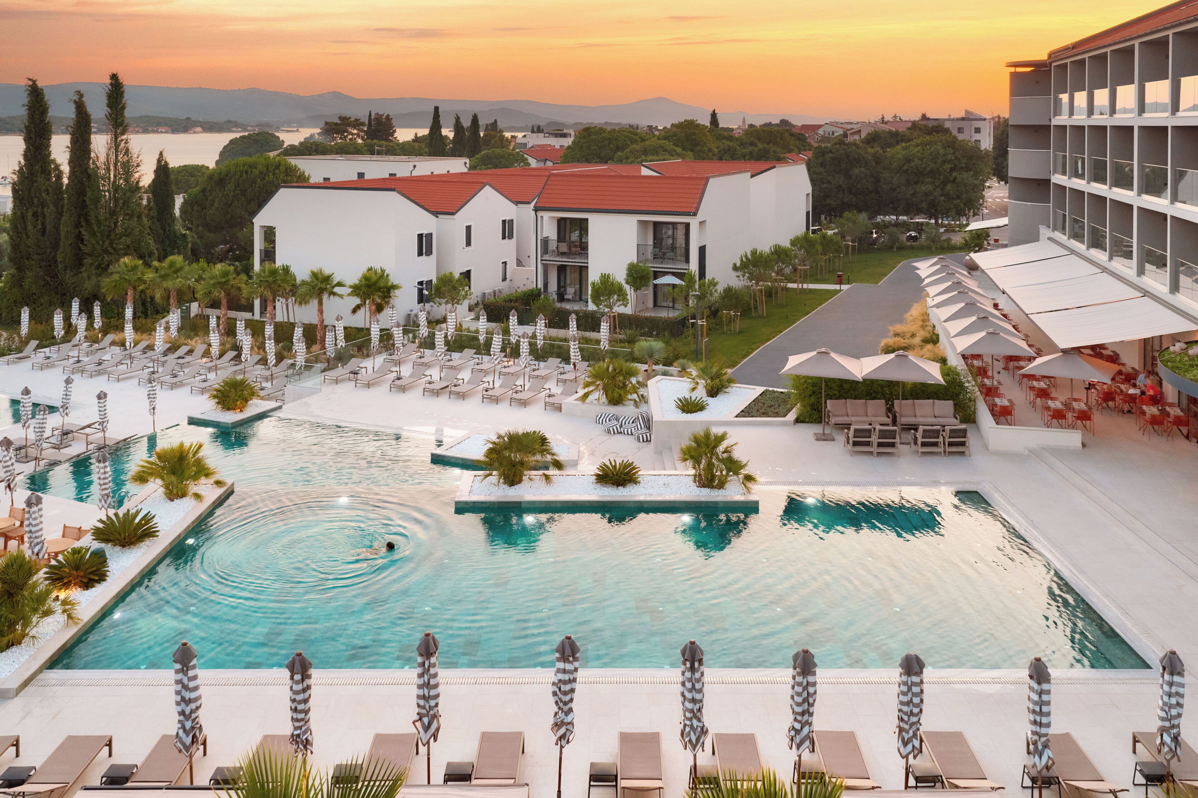 A resort with a swimming pool, lounge chairs, and a view of the surrounding landscape.