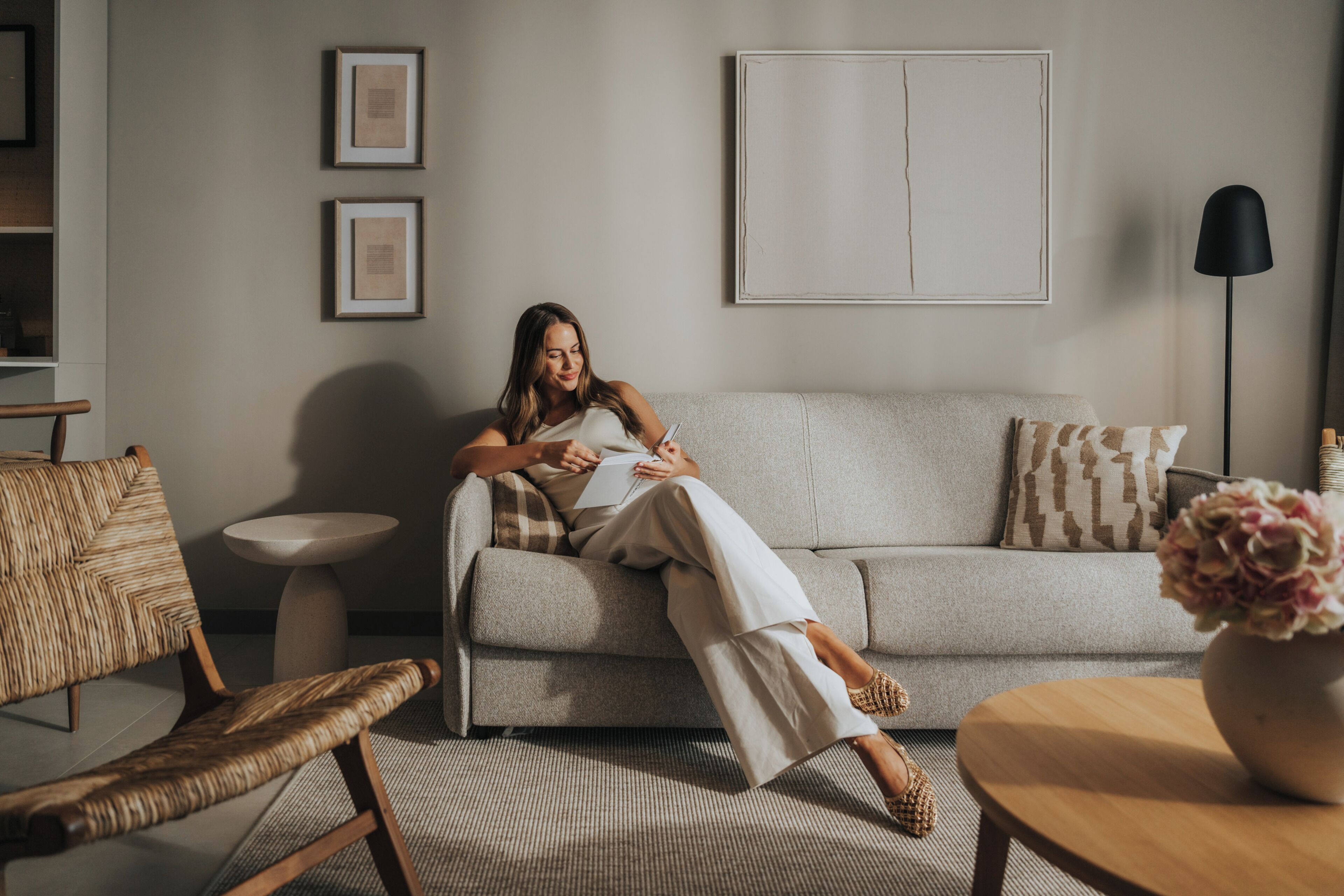 A person sitting on a sofa in a room with a round table, a chair, and a floor lamp.