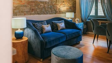 A cozy living room with a stone wall, a blue sofa, a round ottoman, and a dining area with a table and chairs.