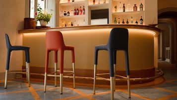 Zona de bar con tres taburetes, una barra con varias botellas y una planta en maceta.