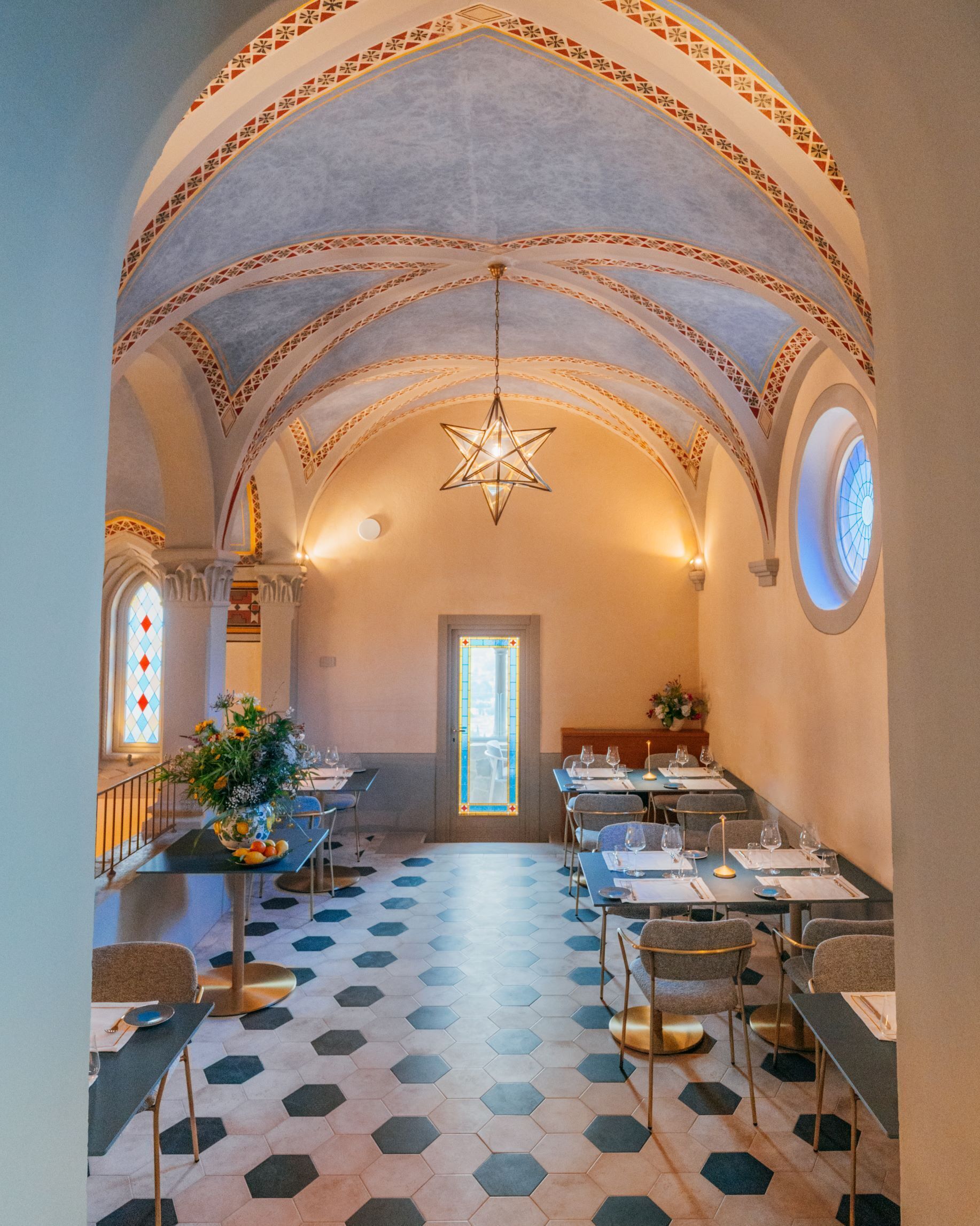 Un área de comedor con piso de patrón hexagonal, mesas dispuestas para comer y una lámpara de araña en forma de estrella.
