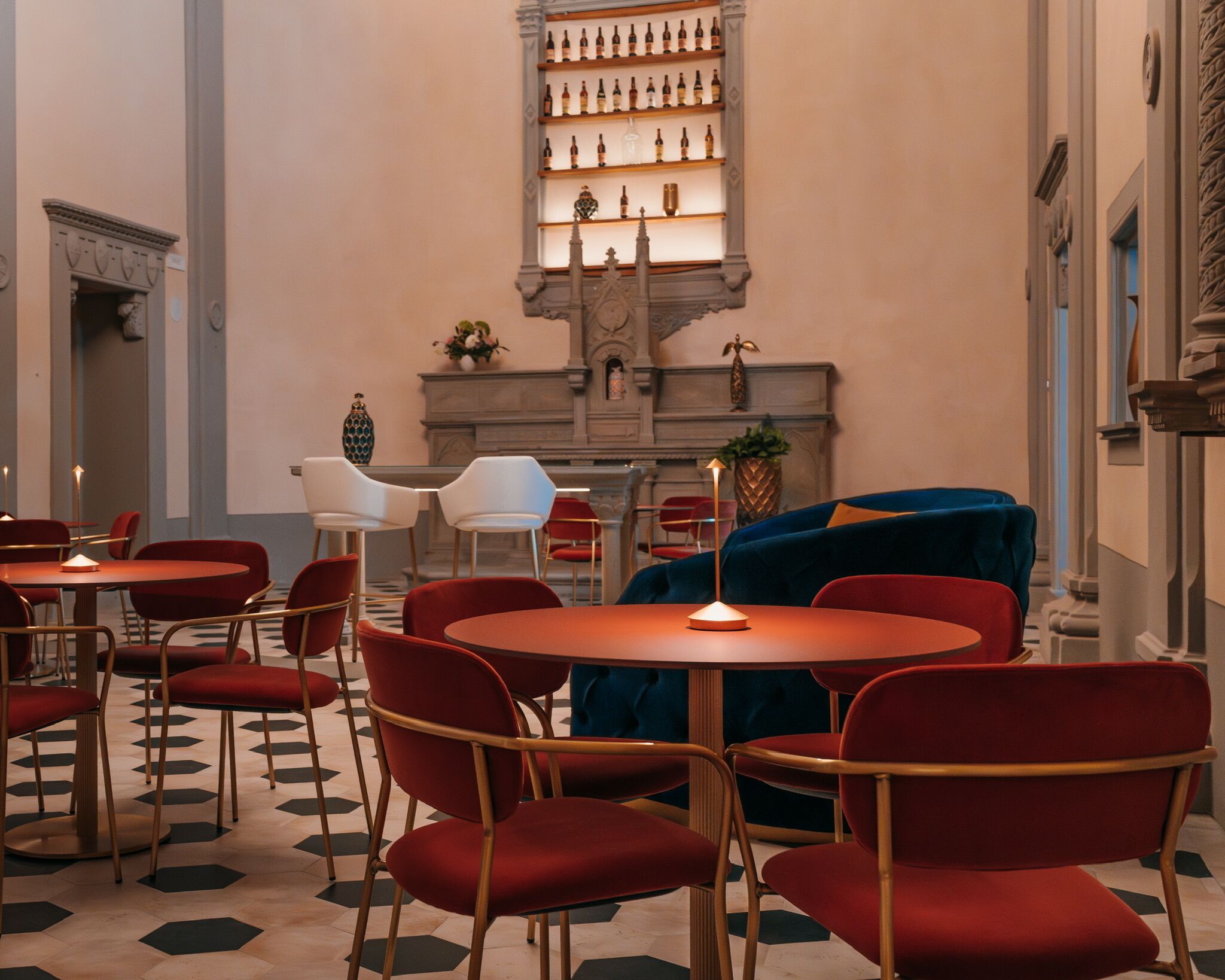 Un hall d’hôtel avec des tables rondes, des fauteuils à revêtement rouge, un canapé bleu et un présentoir à vin accroché au mur.