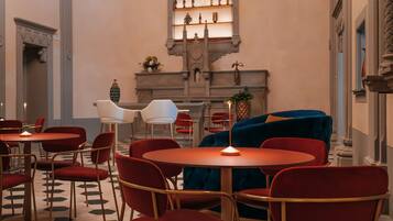 Un hall d’hôtel avec des tables rondes, des fauteuils à revêtement rouge, un canapé bleu et un présentoir à vin accroché au mur.