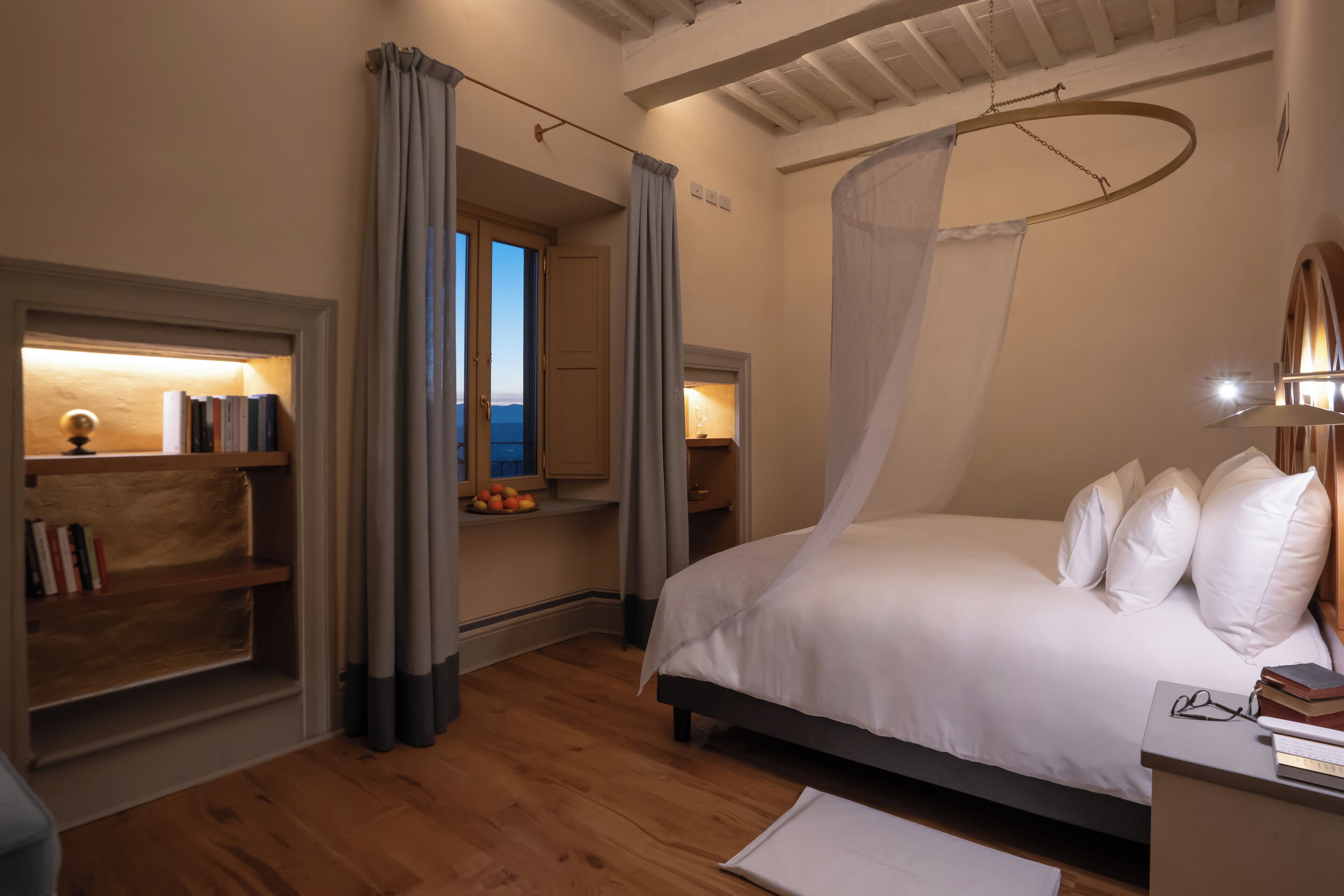 A bedroom with a bed, a bedside table, a bookshelf, and a window with curtains.