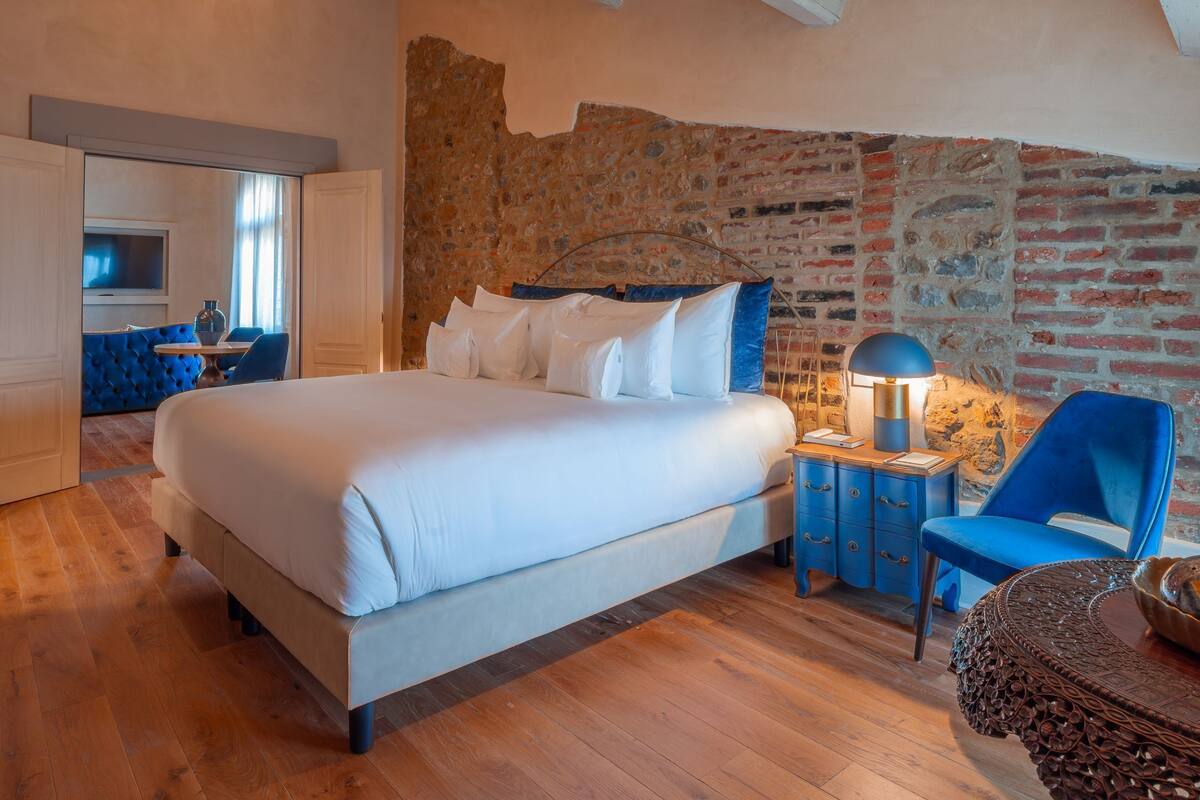 A bedroom with a large bed, a stone wall, and a wooden ceiling.