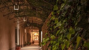 A corridor with a stone wall covered in ivy, a series of hanging lanterns, and a door at the end. - La Monastica Resort & Spa (Buggiano)