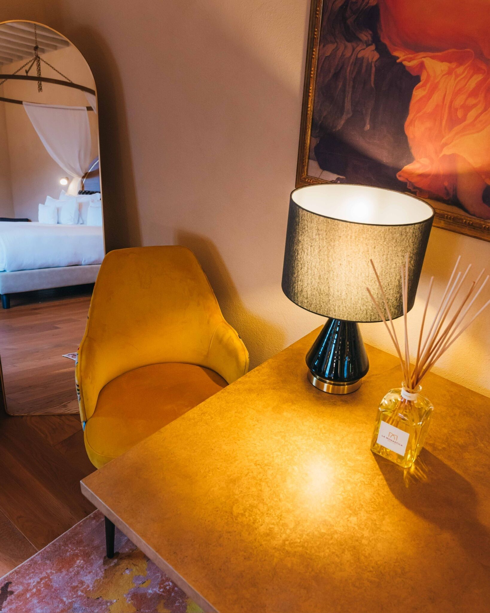 Una habitación con un sillón amarillo, una mesa con lámpara y un difusor de aroma de juncos.