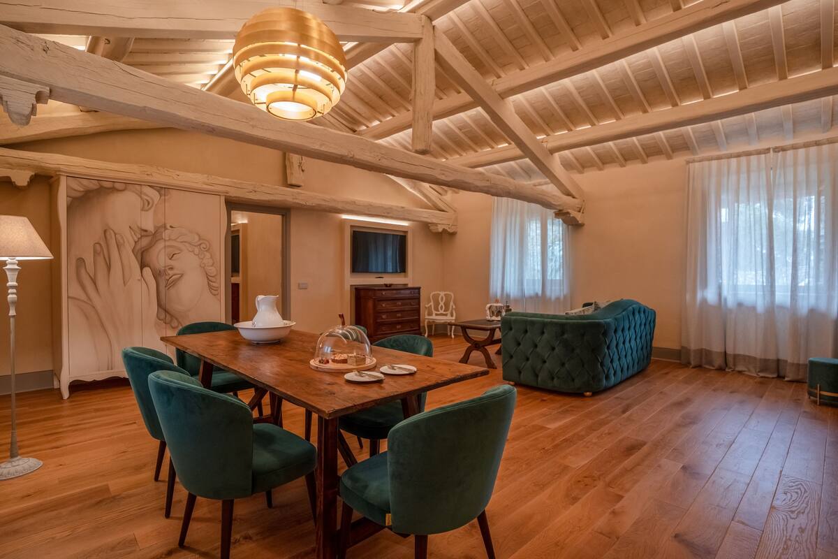 A spacious dining area with a wooden table and green chairs, a green sofa, and a chandelier.