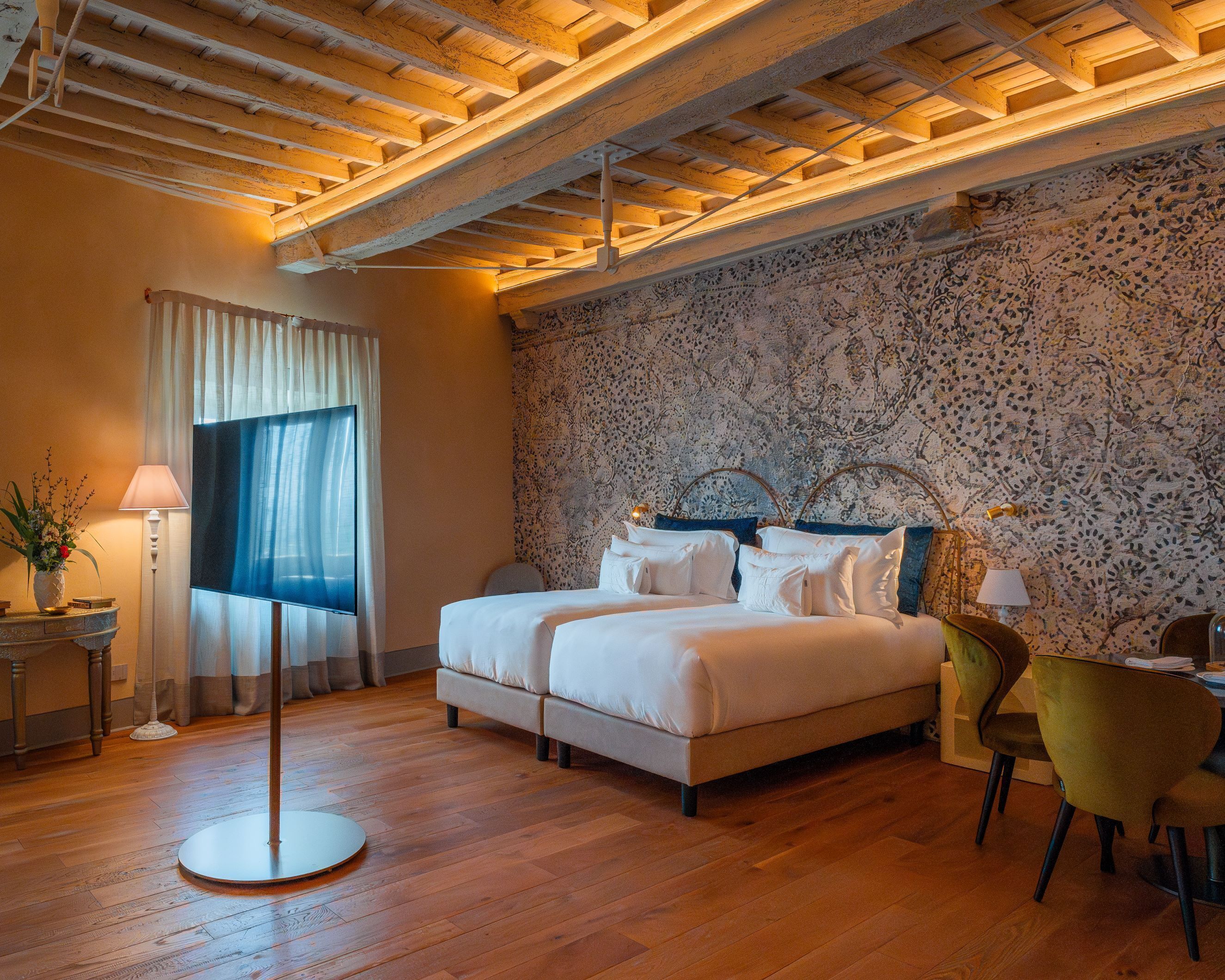 Una habitació d'hotel amb llit, escriptori, cadira, làmpada i una finestra gran amb cortines.